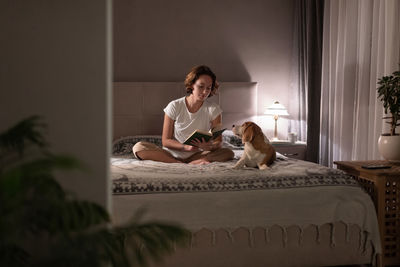 Woman with dog sitting on bed at home