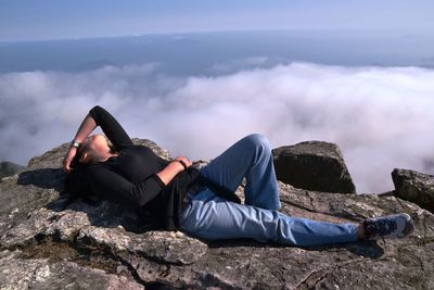 Person sitting on rock against cloudy sky