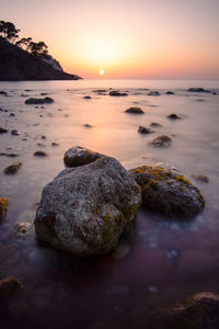 Rocks in sea against sky during sunset