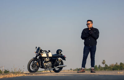 Motorcycle driver in a helmet and leather jacket stands on the road next to a sports motorcycle