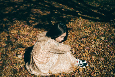 Side view of mid adult woman looking away while sitting on field in park during autumn