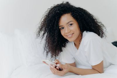 Portrait of smiling young woman using mobile phone while lying on bed