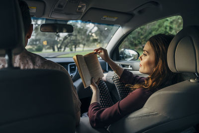 Wife reading book while traveling with husband in car