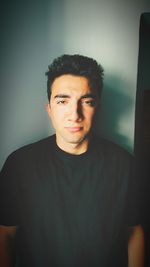 Portrait of young man standing against wall at home