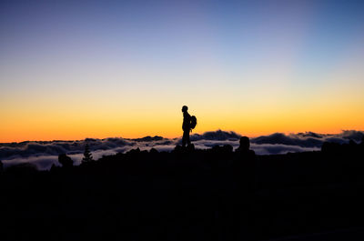 Silhouette hiker standing peak by cloudscape against sky during sunset