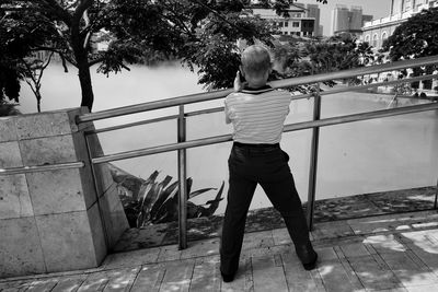 Rear view of man standing by railing against trees