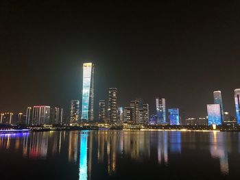 Illuminated buildings by river against sky at night