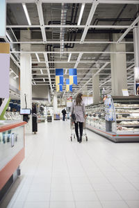 Rear view of woman pushing shopping cart at supermarket