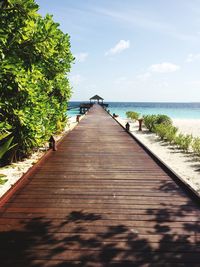 Wooden boardwalk leading towards sea against sky