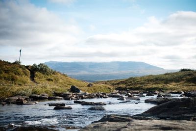 Scenic view of river against sky with clouded mountain in background