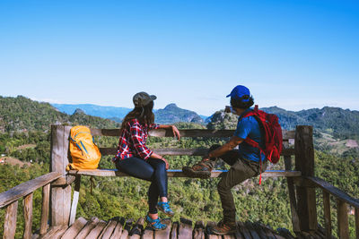 People sitting on mountain against clear sky