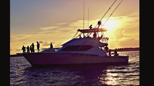 People on boat in sea against sky during sunset