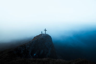 View of religious cross on mountain against fog