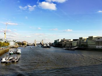 Boats in river by buildings in city against sky