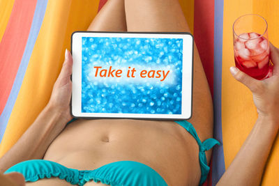 Midsection of young woman wearing bikini using digital tablet while resting on towel outdoors