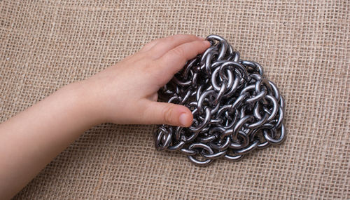Close-up of human hand holding chain over jute