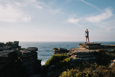 Man standing on rock by sea against sky