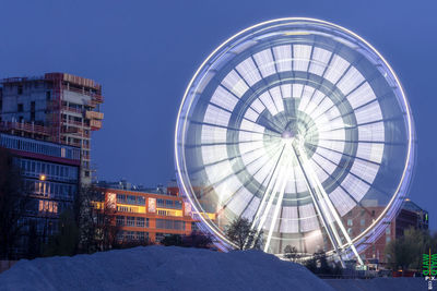 Illuminated ferris wheel in city against clear sky