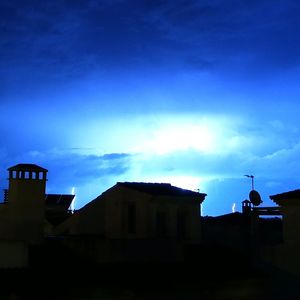 Low angle view of silhouette buildings against blue sky