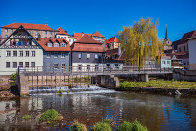 Buildings by river against blue sky