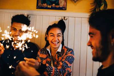 Cheerful young multi-ethnic friends sitting with burning sparklers at restaurant