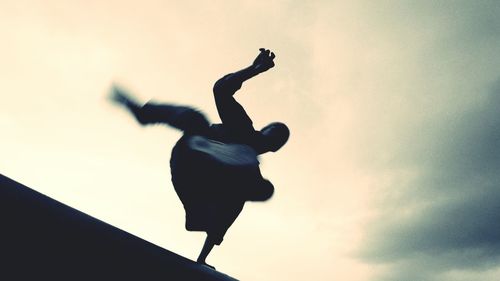 Low angle view of young man jumping against sky