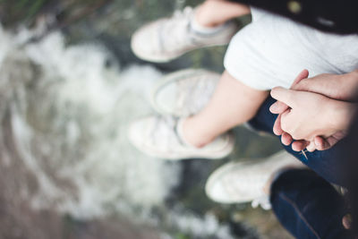 Low section of couple holding hands over sea