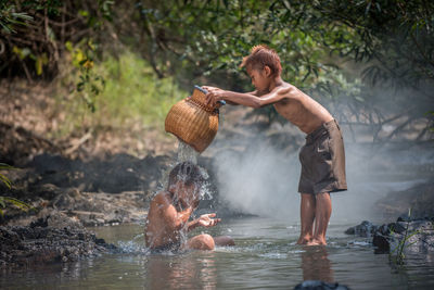 Side view of shirtless boy holding water in river