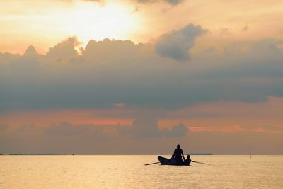 Silhouette men on boat sailing in sea against sky during sunset