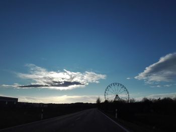 Road amidst silhouette landscape against blue sky