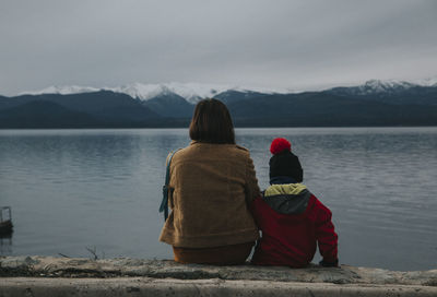 Rear view of woman looking at lake against mountain range