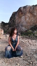 Woman looking away while sitting on rock against clear sky