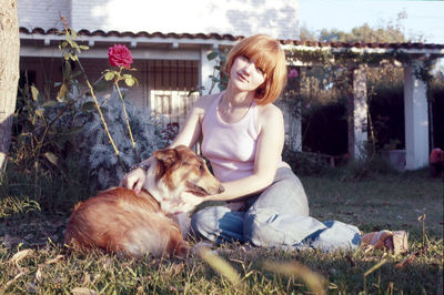Portrait of young woman with dog sitting on field