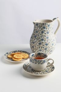 A cup of tea on a small plate with soft focus of jar and biscuits in behind on white table
