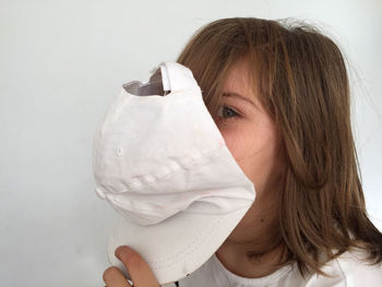 Portrait of girl holding cap against white wall