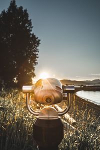 Coin-operated binoculars on field against sky during sunset