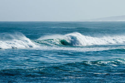 Scenic view of wave rushing sea against clear sky