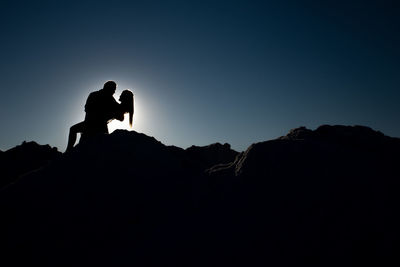 Silhouette people standing on rock against sky