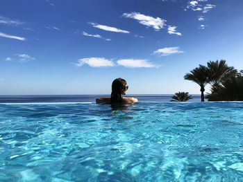 Rear view of woman swimming in infinity pool against sky