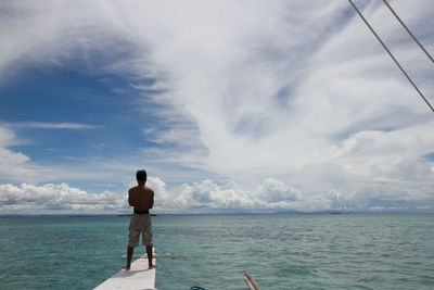 Rear view of man standing at beach against sky