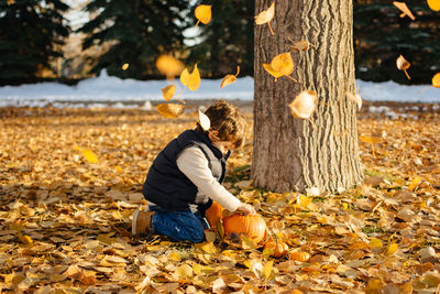 Side view of boy holding pumpkin on field during autumn