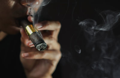 Close-up of man smoking electronic cigarette against black background
