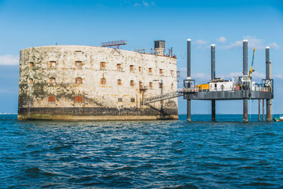 View of factory by sea against clear blue sky