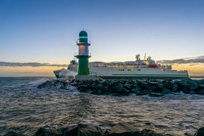 Lighthouse by sea against sky during sunset