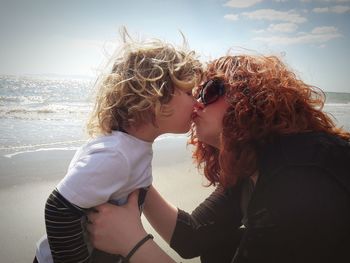 Mother and son kissing at beach against sky