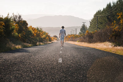 New zealand, north island, rotorua, rear view of young man walking on road in bay of plenty