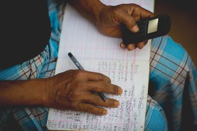 Midsection of man doing calculation with book and mobile phone at home