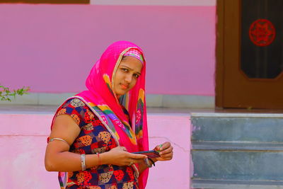 Portrait of young woman standing against pink umbrella