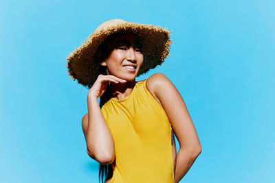 Portrait of young woman wearing hat against clear blue background