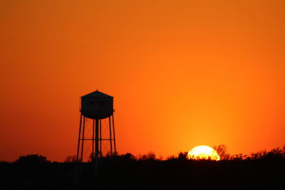 Silhouette water tower against orange sky